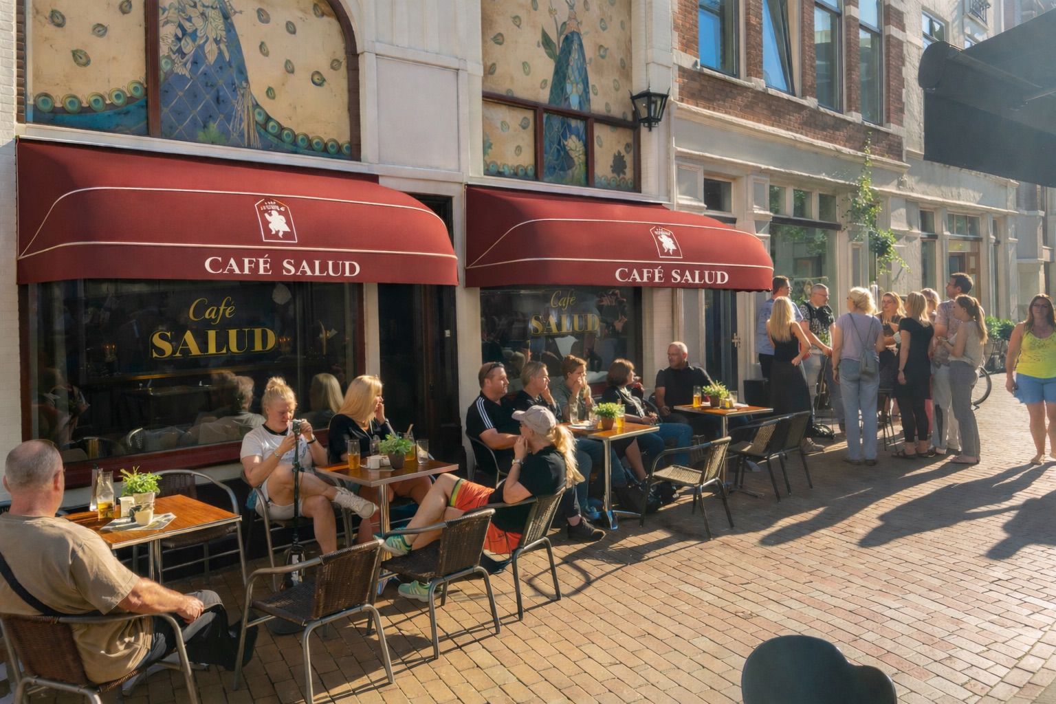 Zonnig terras van Cafe Salud met gasten onder de rode luifels in Groningen